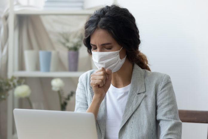 Unhealthy female employee in medical mask cough at workplace