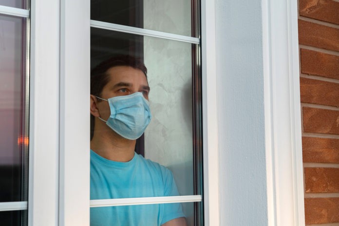 Young man in medical mask is looking out window
